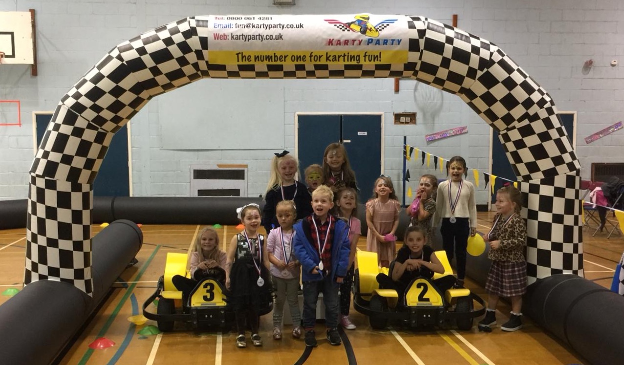 Group of children at a go kart party posing with karts on an iinflatable track